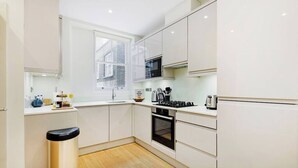 Una cocina moderna con armarios blancos, un basurero de acero inoxidable, una ventana y un horno empotrado.