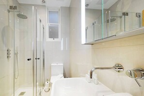 Ett modernt badrum med en dusch som är avskärmad med glasväggar, en vit tvättställ med kromade detaljer och en stor spegel ovanför tvättstället.
