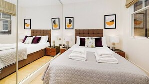 Moderni hotellihuone, jossa on suuri sänky, kaksi yöpöytää, peili ja taideteoksia seinillä.