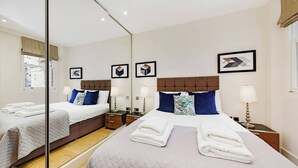 A hotel room with two beds, a large mirror, and framed artwork on the walls. - PBC | Luxury One Bedroom Apartment in Central London, Fitzrovia GT8 (London)