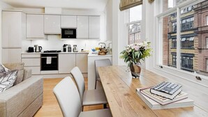 A modern kitchen with white cabinets, a microwave, and a dining area with a wooden table and chairs. - PBC | Luxury One Bedroom Apartment in Central London, Fitzrovia GT8 (London)