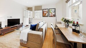 A modern living room with a sofa, TV, and dining area with a table and chairs. - PBC | Modern One Bedroom Apartment in Soho GT8 (London)