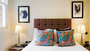 A hotel room with a large bed, two side tables, two lamps, and two framed artworks on the wall. - PBC | Modern One Bedroom Apartment in Central London, Fitzrovia GT10 (London)