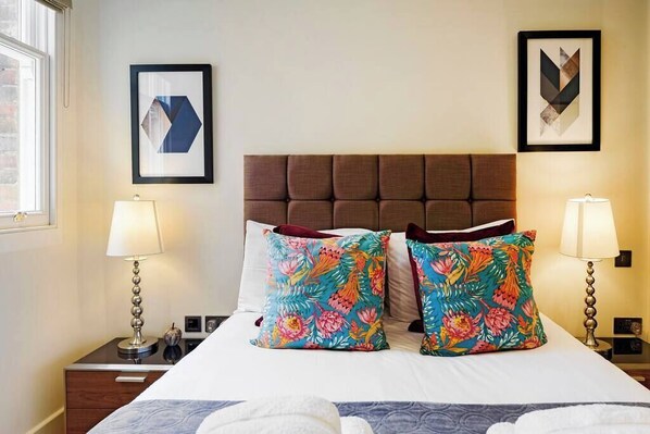 Ein Hotelzimmer mit einem großen Bett, zwei Nachttischen, zwei Lampen und zwei gerahmten Kunstwerken an der Wand.