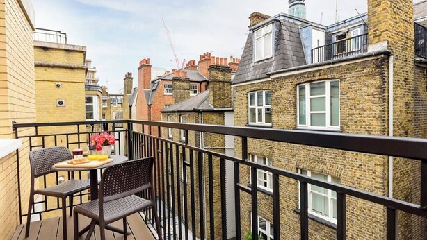A balcony with a table and chairs, overlooking a street with traditional brick buildings and a construction crane in the background. - PBC | Luxury One Bedroom Apartment in Central London, Fitzrovia (GT12) (London)