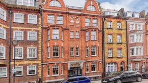 A row of red brick townhouses with uniform window patterns and a central entrance. - PBC | Luxury One Bedroom Apartment in Soho GT13 (London)