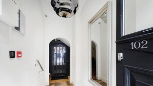 A hallway with a black door labeled "102," a fire alarm, and a security camera. - PBC | Luxury One Bedroom Apartment in Soho GT13 (London)