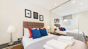 A hotel room with a large bed, bedside tables, a mirror, and artwork on the wall. - PBC | Luxury One Bedroom Apartment in Soho GT13 (London)