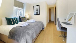 Une chambre d’hôtel moderne équipée d’un lit, d’un bureau, d’un ordinateur portable et d’un tableau représentant une tour de l’horloge.