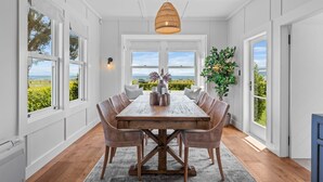 A dining area with a wooden table, wicker chairs, and a view of the outdoors. - Drift @ 5 Mile Bay (Taupo)