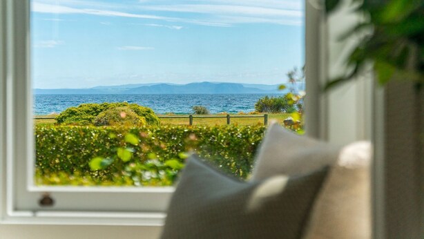 A window with a view of a coastal landscape, including a body of water and distant mountains. - Drift @ 5 Mile Bay (Taupo)