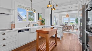 A modern kitchen with white cabinetry, a wooden island, pendant lighting, and a view to the outdoors. - Drift @ 5 Mile Bay (Taupo)