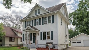A two-story white house with green shutters, a front porch, and a garage.