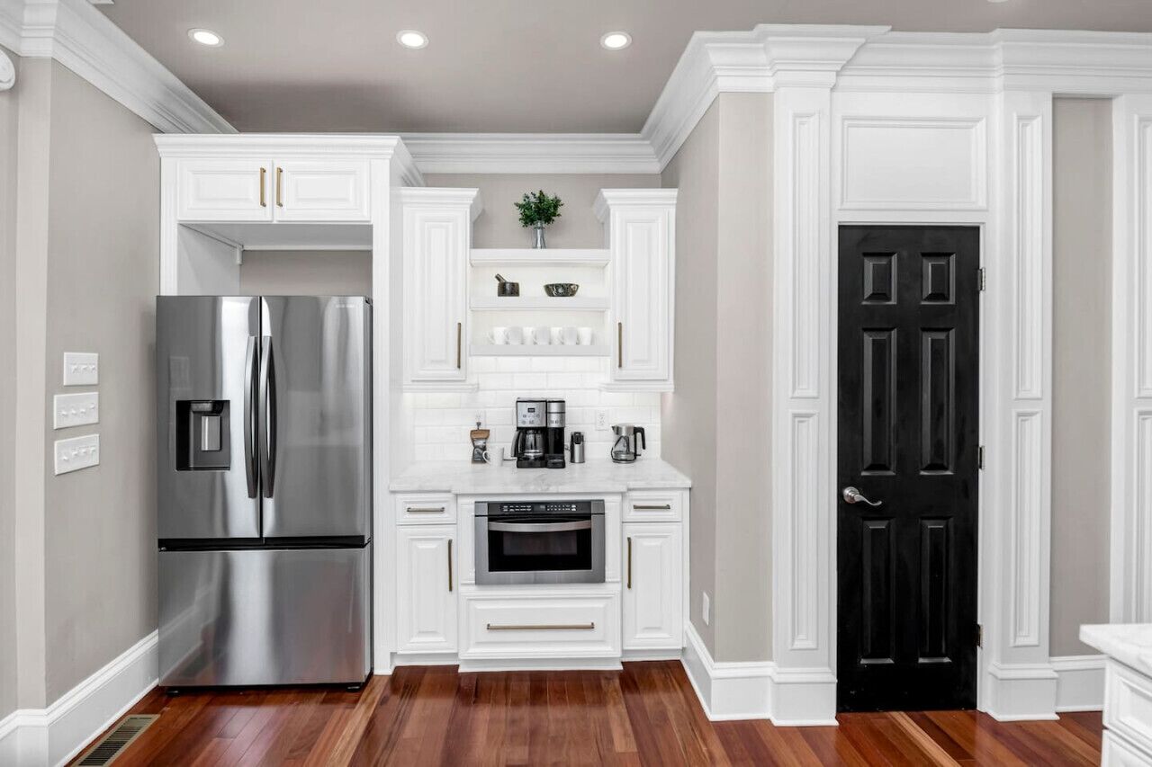 A kitchen with white cabinetry, a stainless steel refrigerator, an oven, and a black door.