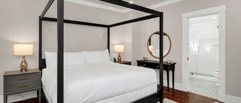 Un lit à baldaquin avec du linge de lit blanc, deux tables de chevet avec des lampes, un ventilateur de plafond et un miroir au mur.
