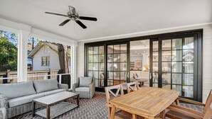Un patio al aire libre con una mesa y sillas de madera, un sofá gris y una silla de mimbre.