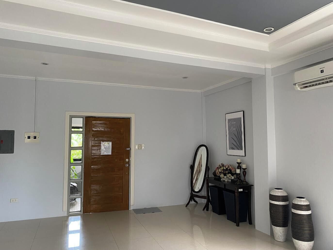 Un pasillo espacioso con una puerta de madera, un cuadro enmarcado en la pared y dos jarrones grandes sobre una mesa.