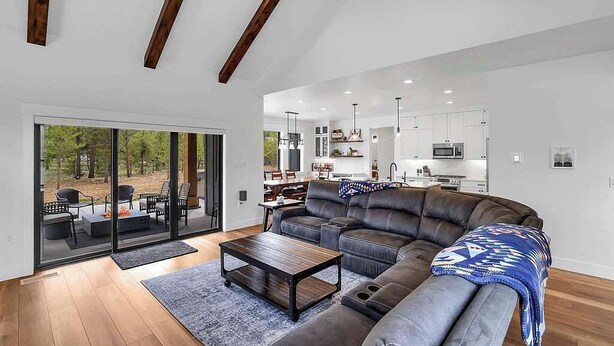 Un salon moderne avec un canapé d’angle, une table basse et un coin repas visible à travers des portes vitrées.