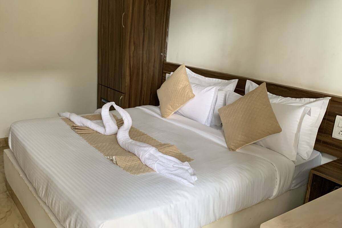 A neatly made bed with white linens and beige pillows, a wooden wardrobe, and a marble floor.
