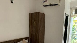 Une chambre d’hôtel équipée d’un lit, d’une armoire, d’un appareil de climatisation et offrant une vue sur la verdure environnante.