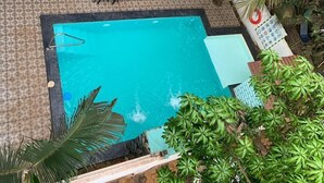 Un espace piscine aménagé sur le toit, avec une piscine bleue, entourée de palmiers et dotée de coins salon extérieurs.