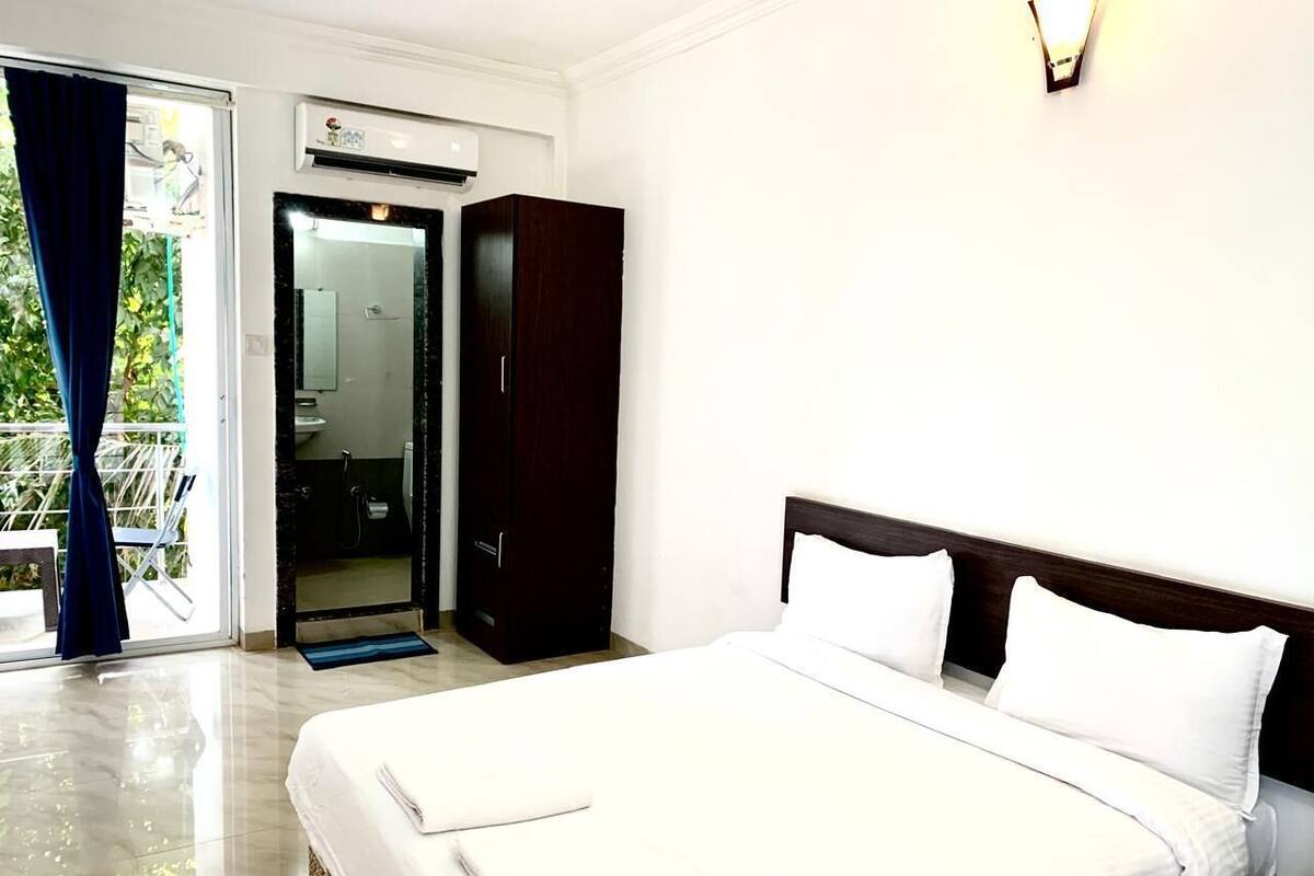 A hotel room with a bed, a wardrobe, a bathroom with a shower, and a balcony with curtains.