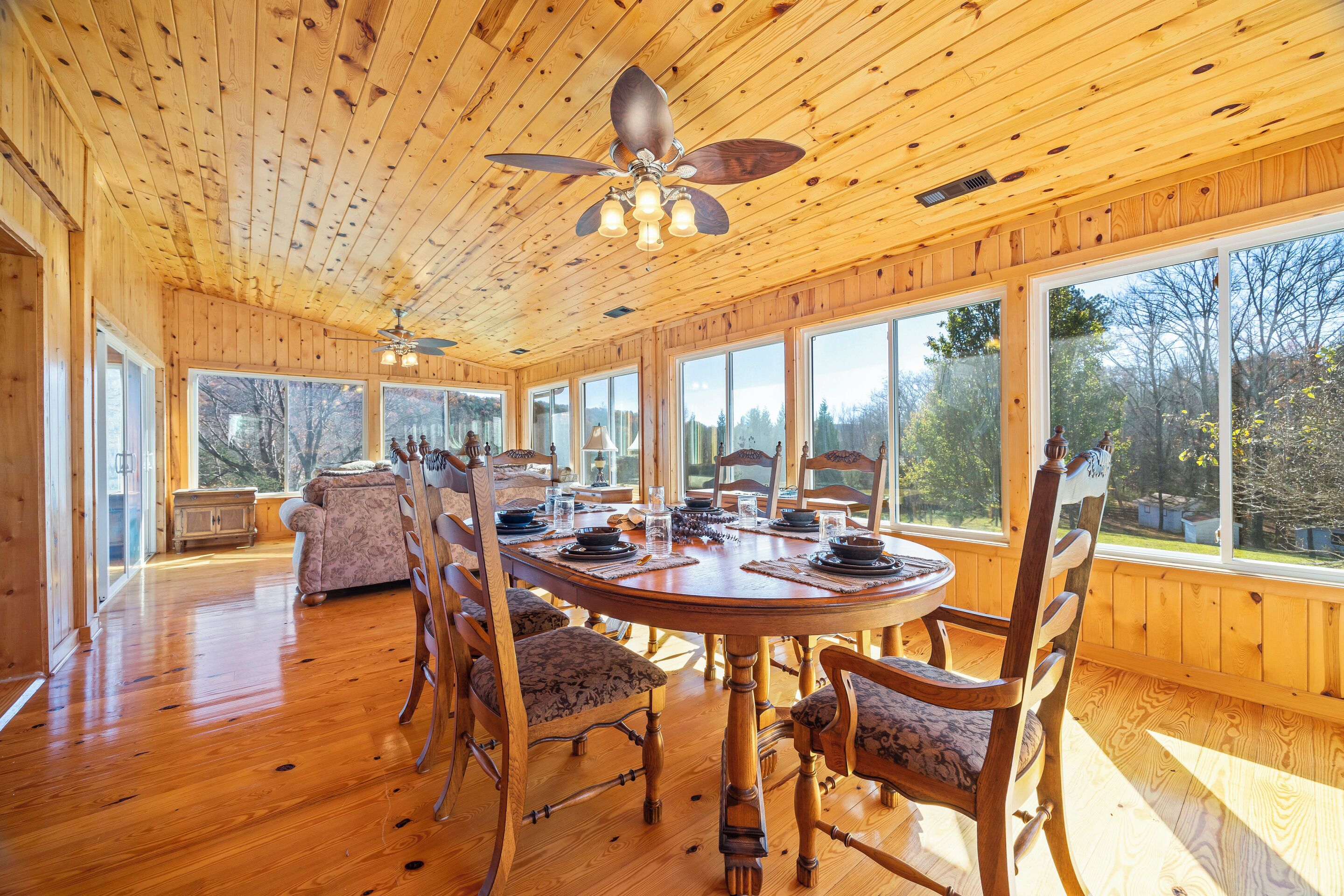 Une salle à manger en bois avec une grande table, des chaises et un ventilateur de plafond.