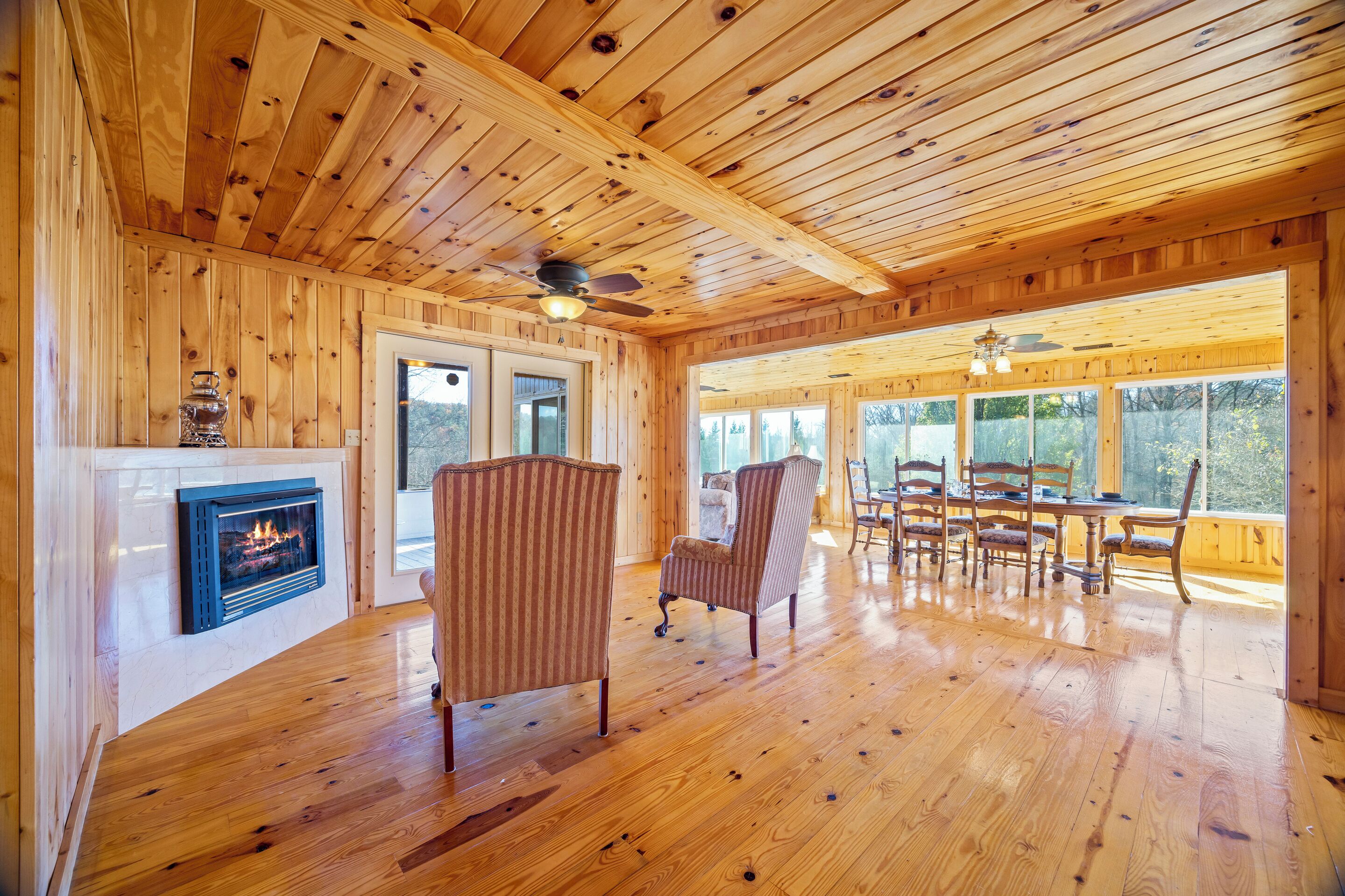 L’intérieur d’un chalet en bois comprend une cheminée, un plancher en bois et un coin repas avec des chaises et une table.