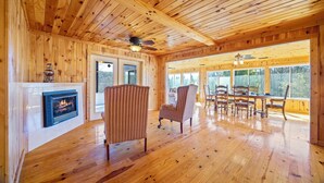Interior de una cabaña de madera con chimenea, pisos de madera y un comedor con sillas y una mesa.