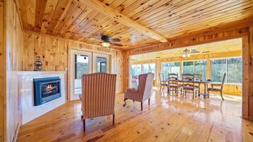 L’intérieur d’un chalet en bois comprend une cheminée, un plancher en bois et un coin repas avec des chaises et une table.