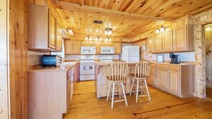 Cocina con paneles de madera, electrodomésticos integrados, una isla central con sillas y piso de madera.