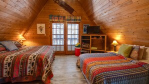 A cozy attic bedroom with two beds, a television, and a small desk area. - Charming 3-bedroom cabin with WiFi in Angel Fire (Angel Fire)