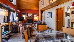A cozy living room with a fireplace, wooden ceiling, and a dining area with a glass table. - Charming 3-bedroom cabin with WiFi in Angel Fire (Angel Fire)