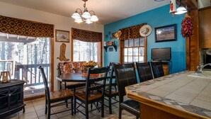 A dining area with a wooden table and chairs, a kitchen counter with a sink, and a television on a wooden cabinet. - Charming 3-bedroom cabin with WiFi in Angel Fire (Angel Fire)
