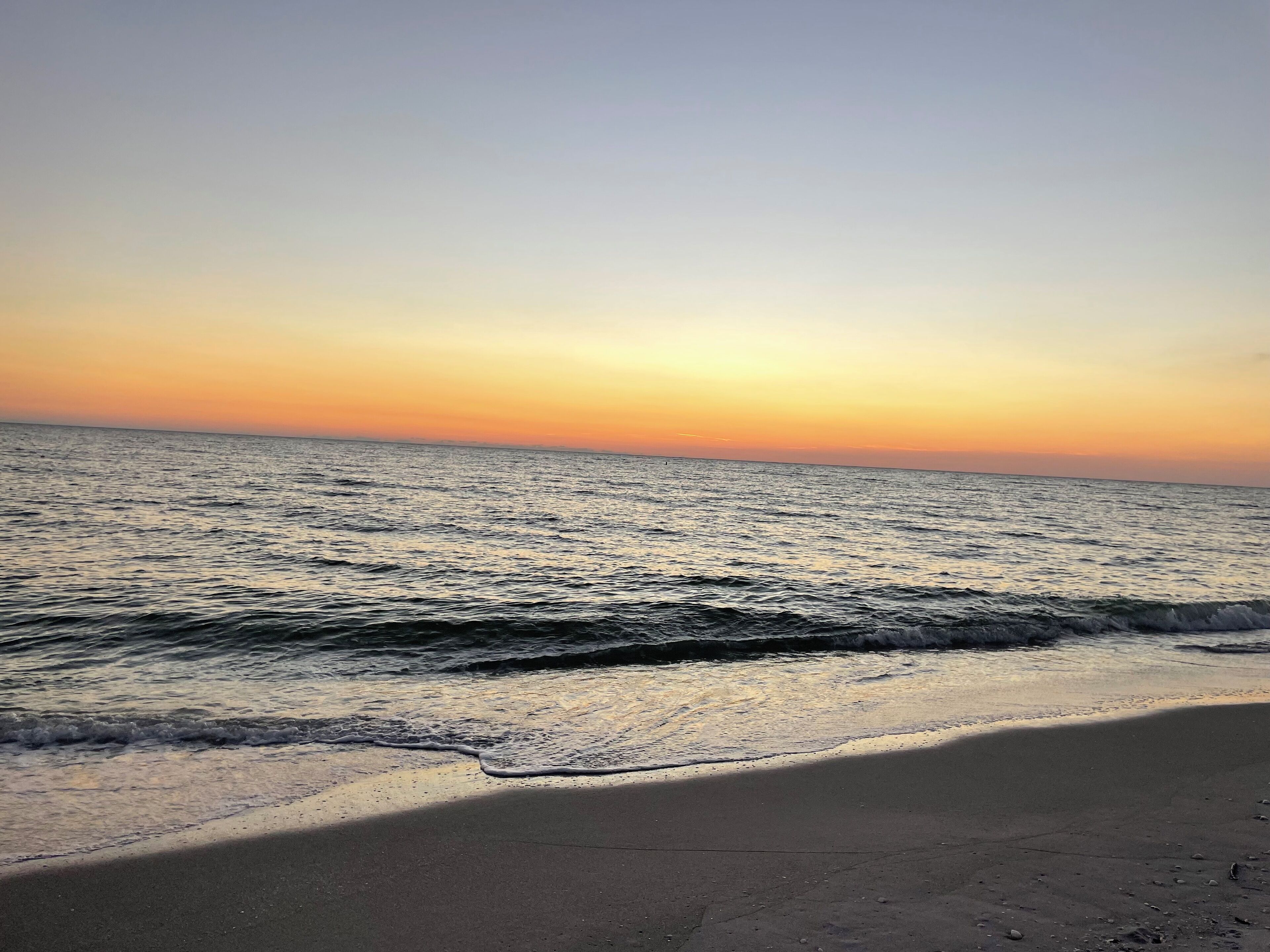 Ein Strand mit ruhigem Meer und klarem Himmel im Sonnenuntergang.