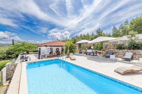 A swimming pool with lounge chairs and umbrellas, surrounded by stone walls and greenery.
