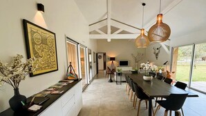 A modern kitchen with a long counter, a dining area with a large table and chairs, and a view of the outdoors through large windows.