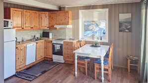A compact kitchen with wooden cabinets, a white countertop, a stove, and a dining table with chairs. - Beach front home in Frosta with WiFi (Frosta)