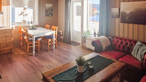 A cozy living room with a red sofa, wooden dining table, and chairs. There is a coffee table with a plant and a rug. - Beach front home in Frosta with WiFi (Frosta)