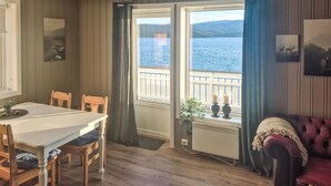 A cozy room with a wooden table and chairs, a red sofa, and a view of a lake through a window with curtains. - Beach front home in Frosta with WiFi (Frosta)