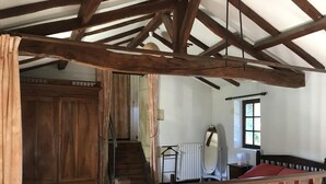 A rustic room with exposed wooden beams, a wooden wardrobe, a bed with a red bedspread, and a window with a view. - Pigeonnier du Rau - GAMARDE LES BAINS (GAMARDE-LES-BAINS)