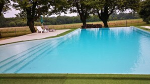 A rectangular swimming pool with a clear blue water surface, surrounded by a well-maintained lawn and a stone wall. - Pigeonnier du Rau - GAMARDE LES BAINS (GAMARDE-LES-BAINS)