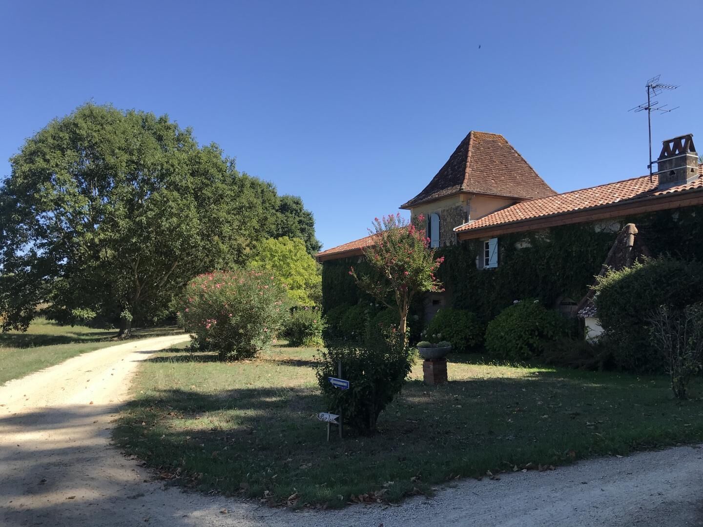 Une maison avec un toit en tuiles, entourée de verdure et bordée d’un chemin de gravier.