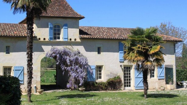 A two-story building with a tiled roof, blue shutters, and a central archway. - Pigeonnier du Rau - GAMARDE LES BAINS (GAMARDE-LES-BAINS)