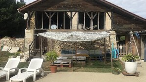 A rustic wooden building with a stone foundation, a covered patio area with white lounge chairs, and a small table. - Pigeonnier du Rau - GAMARDE LES BAINS (GAMARDE-LES-BAINS)