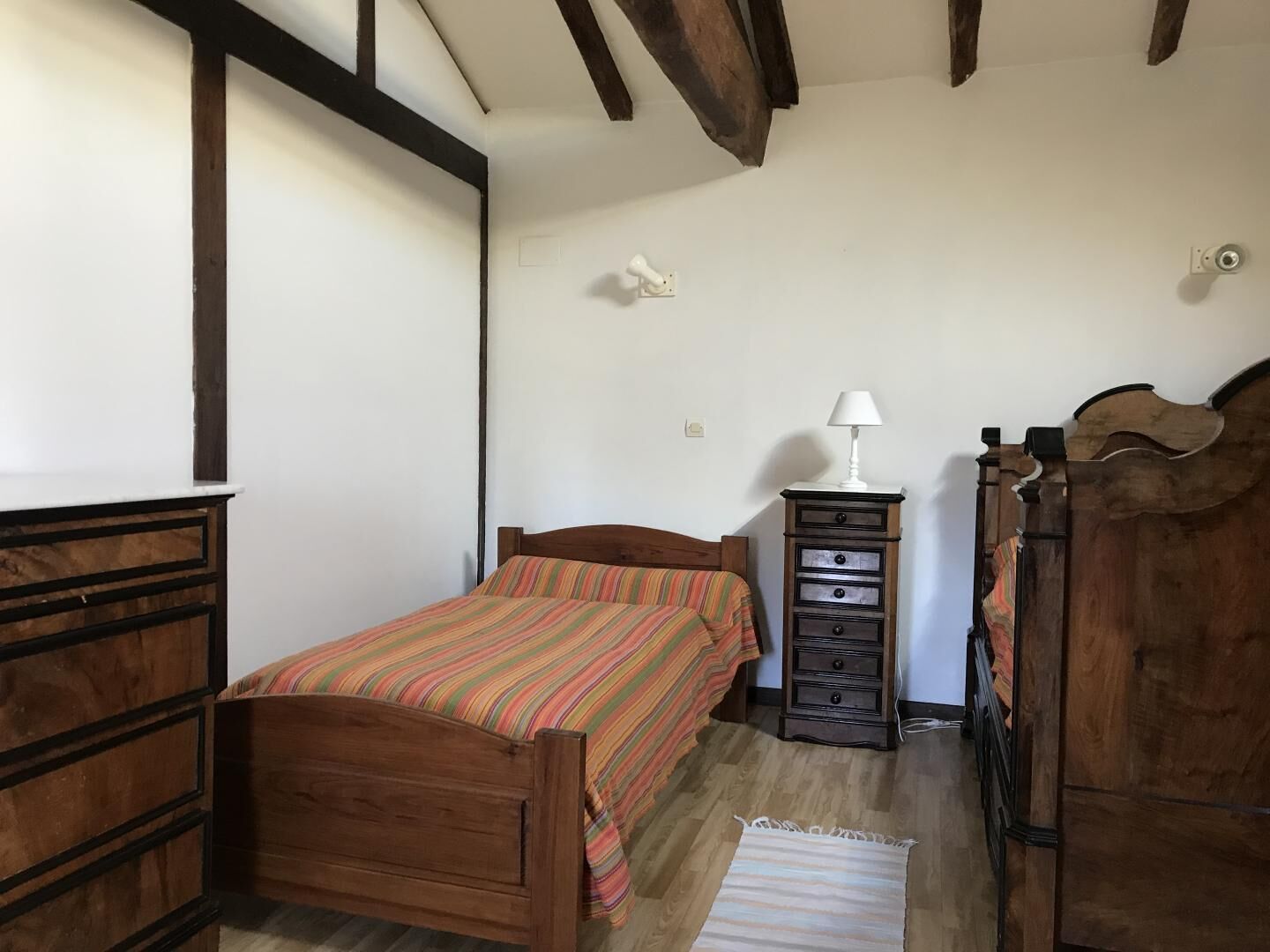 A bedroom with a wooden bed, a dresser, a nightstand, and a lamp.