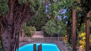 Una piscina rodeada por un muelle de madera y una cerca de madera, con árboles y plantas a su alrededor.
