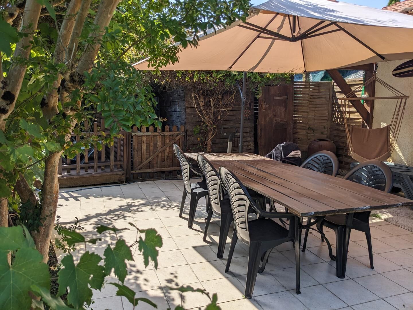 An outdoor patio with a wooden table and chairs, a large umbrella, and a rustic fence.