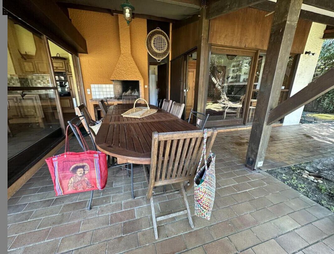 A covered patio with a wooden table and chairs, a wicker basket, and a red bag.
