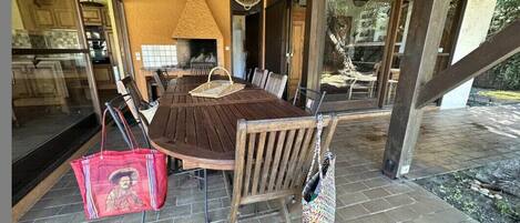 A covered patio with a wooden table and chairs, a wicker basket, and a red bag.